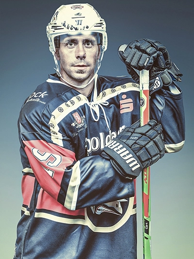 Nahaufnahme eines entschlossenen Eishockeyspielers der Black Dragons aus Erfurt, der in seiner Ausrüstung mit Schläger posiert. Ein kraftvolles Sportporträt von Michael Schalansky.